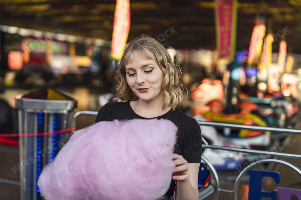 A blonde Spanish female eating cotton candy in an amusement park
