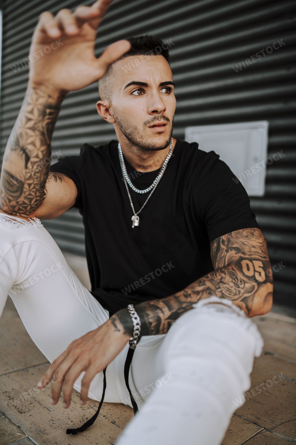 A vertical shot of a young hip confident tattooed male looking to his left sitting on the floor