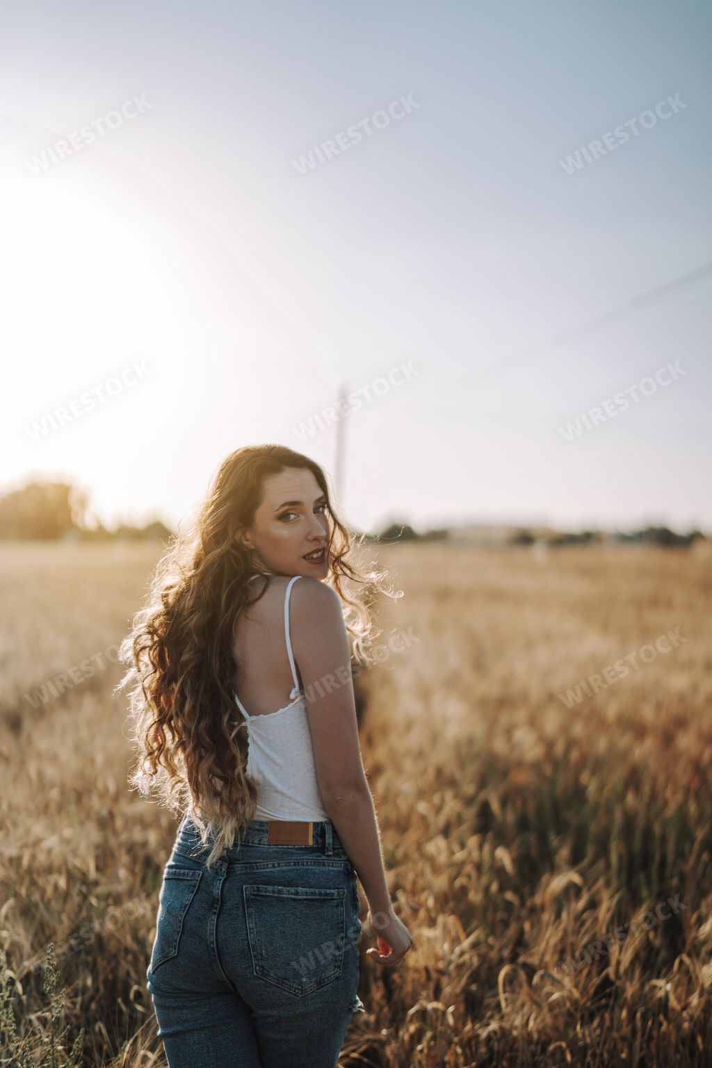 A vertical shot of a sexy Spanish woman with blond hair, looking over her shoulder in a sunny field