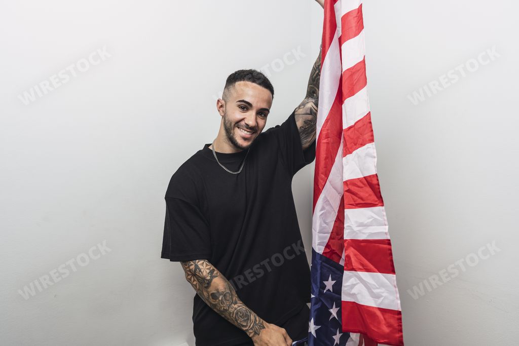 A young proud Hispanic man holding a US flag against a white background