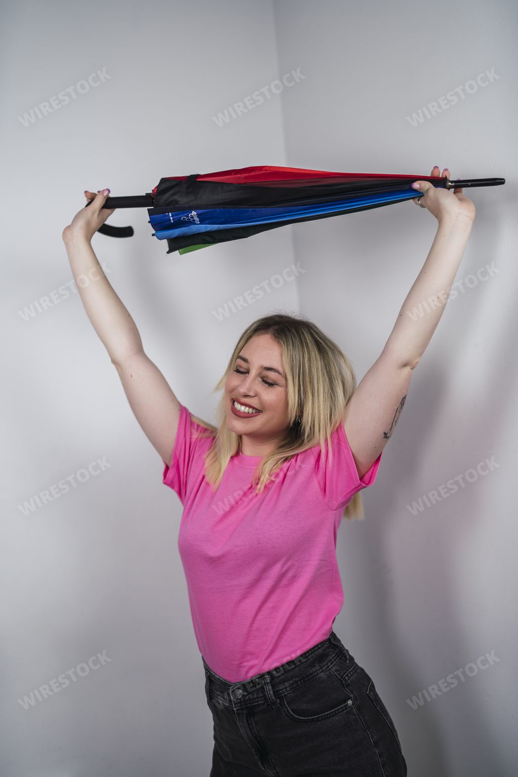 A vertical shot of happy Spanish female with pink shirt holding a rainbow umbrella on white background