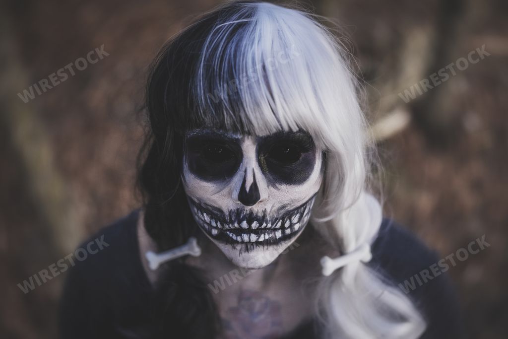A female wearing a skeleton costume and skull makeup on her face in the middle of a creepy forest