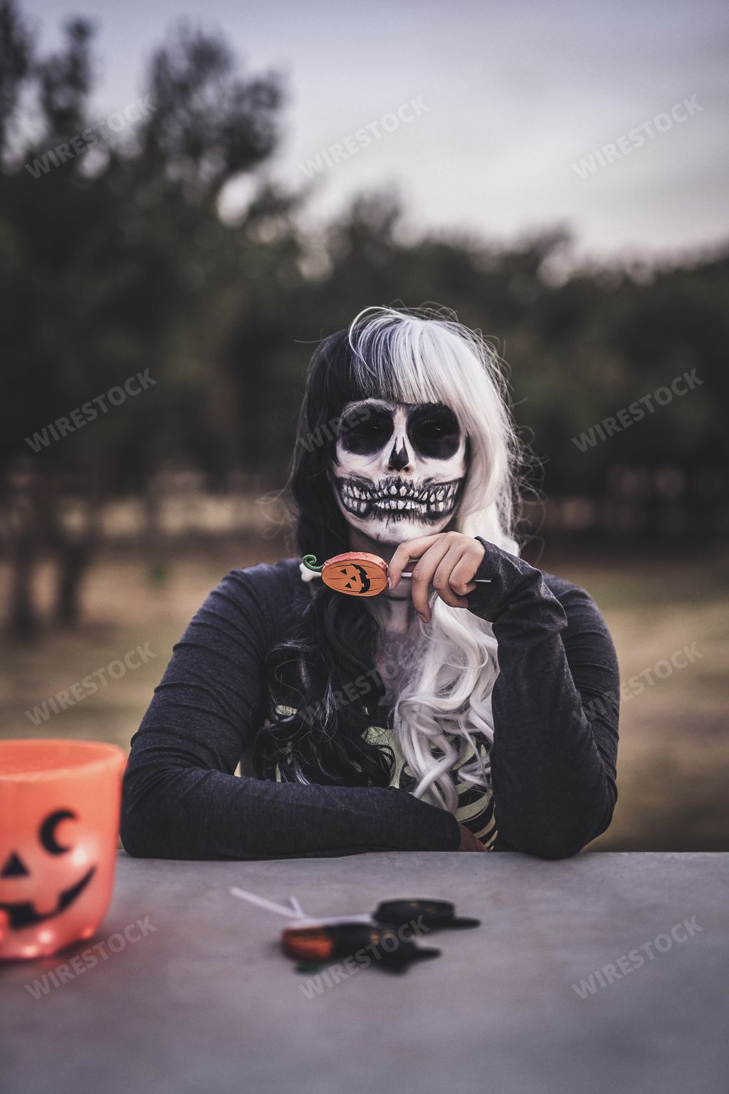A vertical shot of a female wearing a skeleton costume and skull makeup holding some lollipops