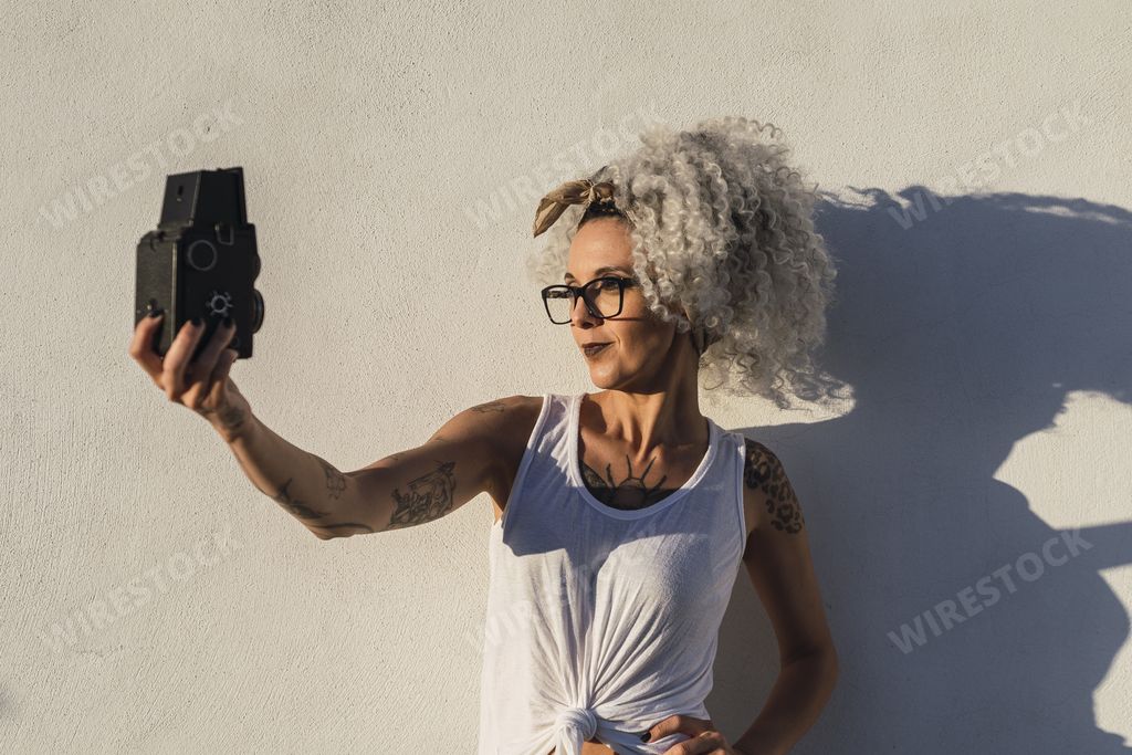 A sexy Caucasian female posing outdoors while taking a selfie on an old camera on a sunny day