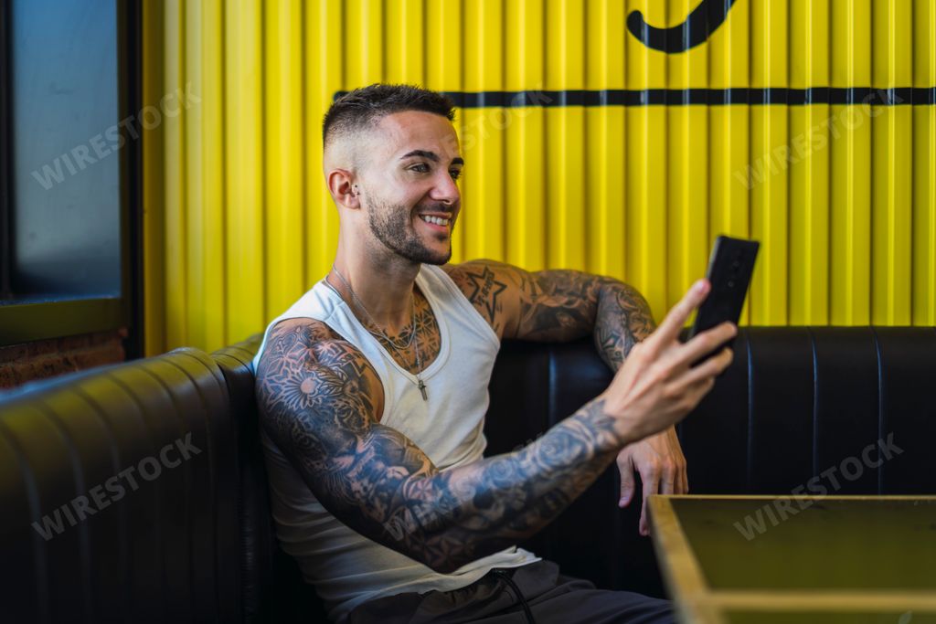 A man sitting on a couch with a smiling face while holding his smartphone