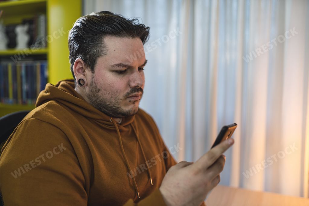 A selective focus shot of a moody cool guy with piercings using his smartphone in a room