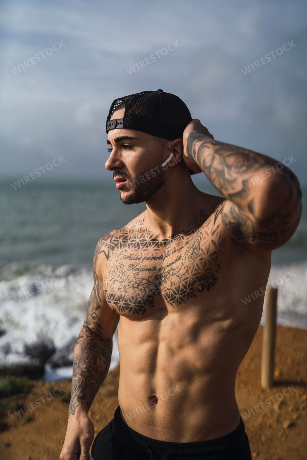 A topless Caucasian man from Spain with tattoos posing in a beach