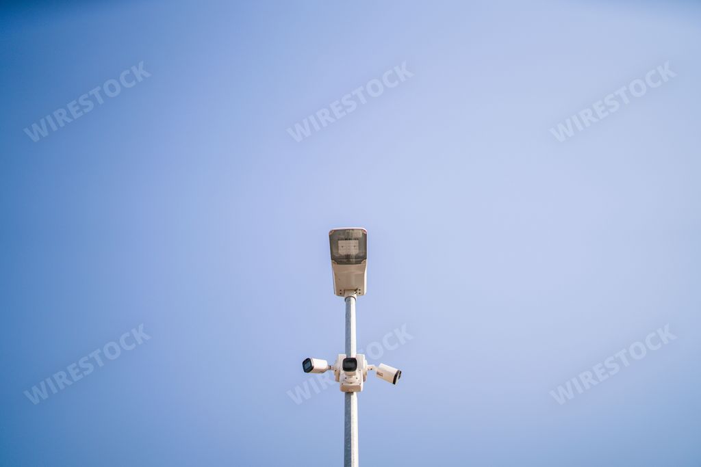 A surveillance camera on a pole in a public place in the background of sky