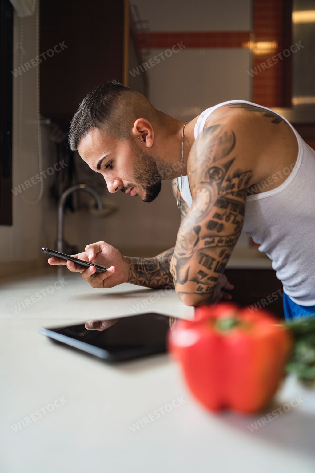 A side angle of a hot tattooed man standing in the kitchen looking in his phone