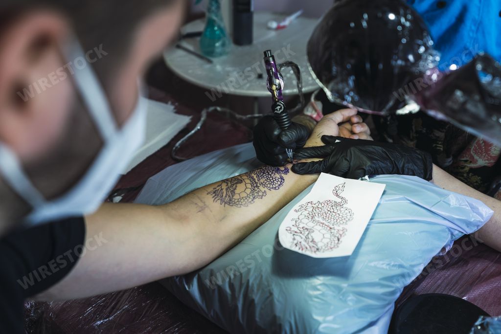 A man wearing a face mask when getting his hand tattooed in a tattoo salon