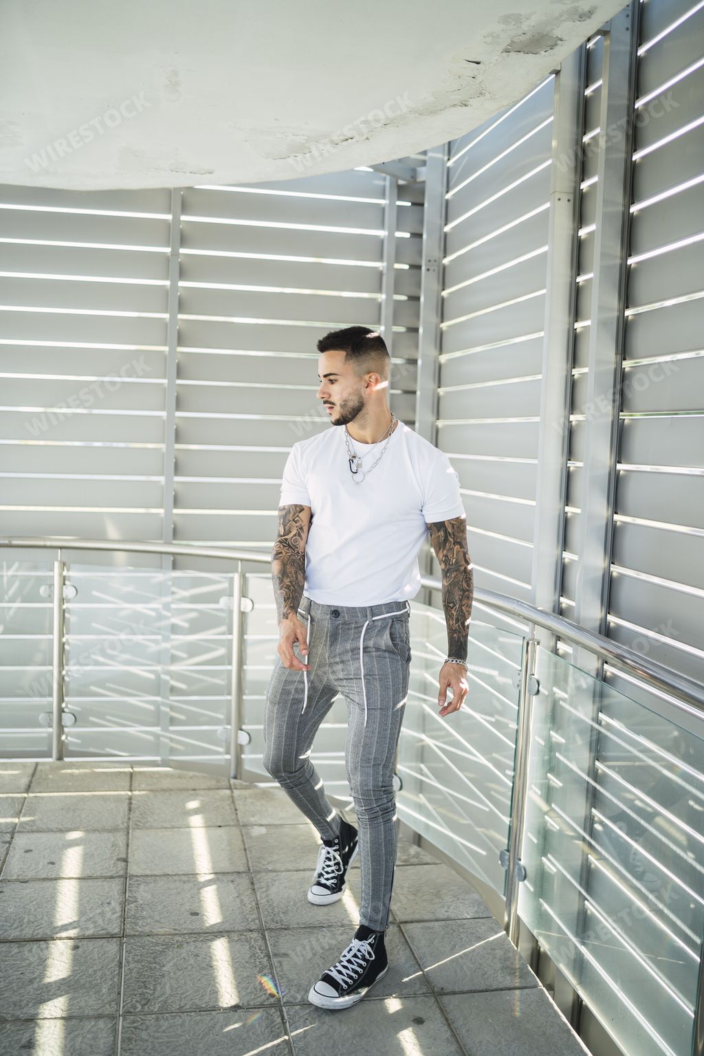 A hot tattooed man wearing a white T-shirt and gray striped pants with canvas shoes