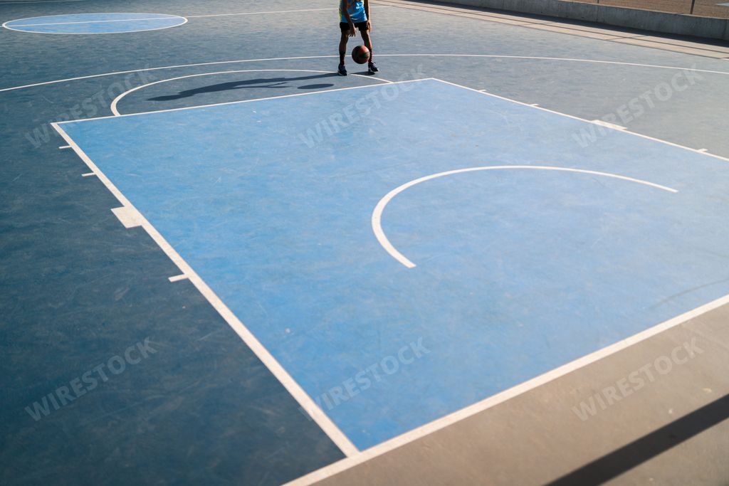 A kid playing basketball on a playground on a sunny morning