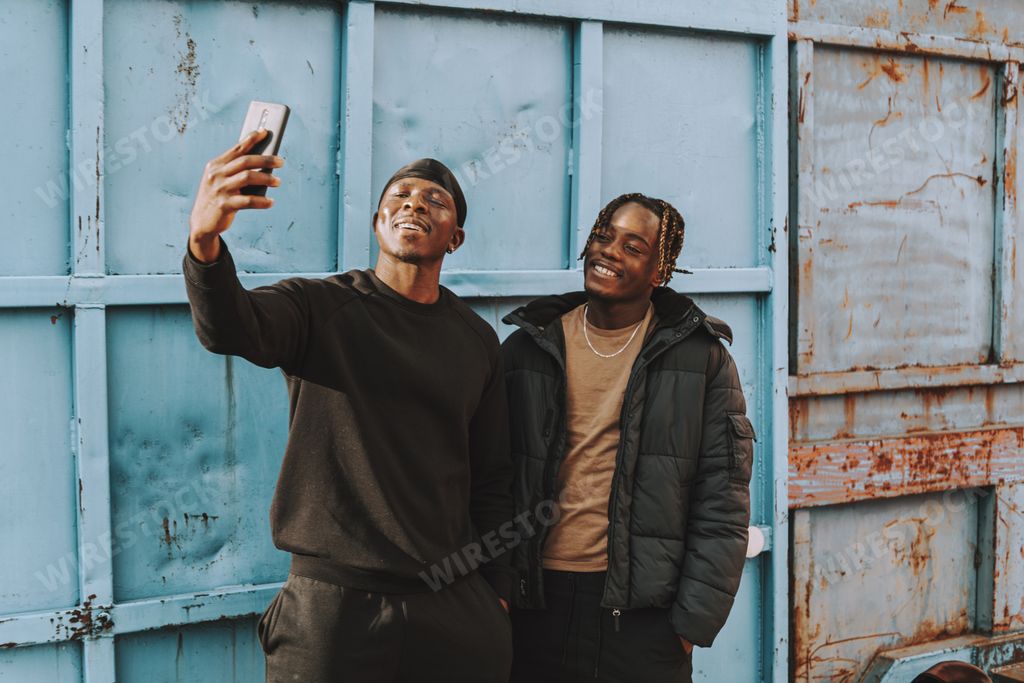 Two happy smiling Black Spanish male friends taking a selfie in front of a blue metal gate