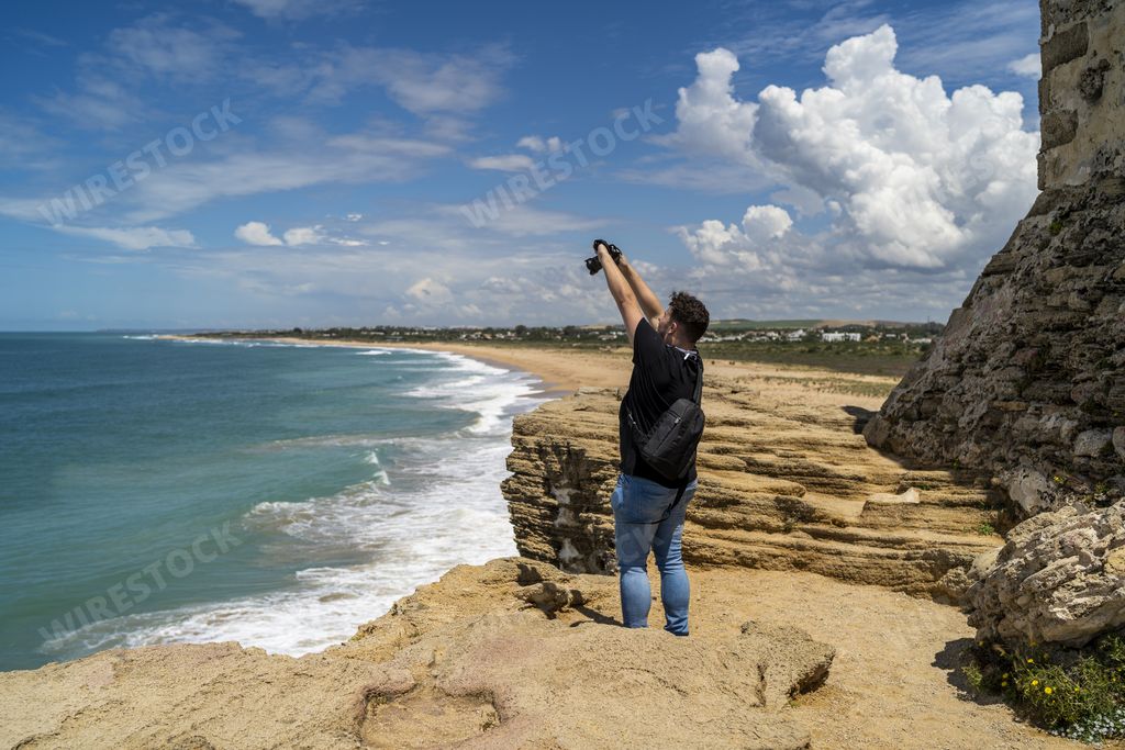 A male photograph taking a picture of the sea surrounded by rocks in Andalusia, Spain
