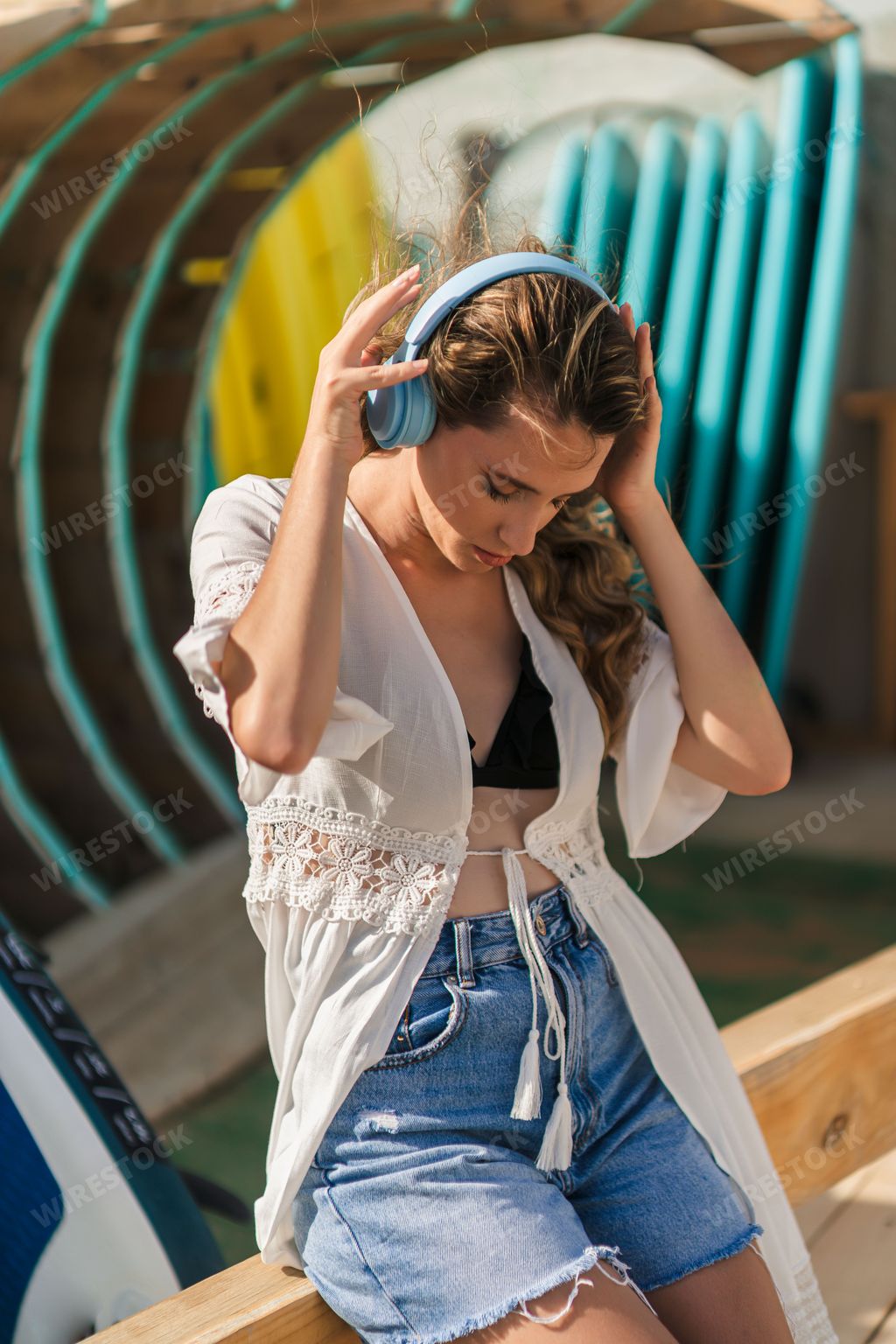 A vertical shot of a young, beautiful Spanish woman with headphones posing by the beach