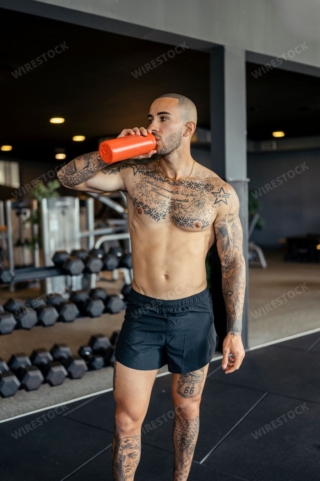 A young, tattooed male with a fit physique poses in a gym