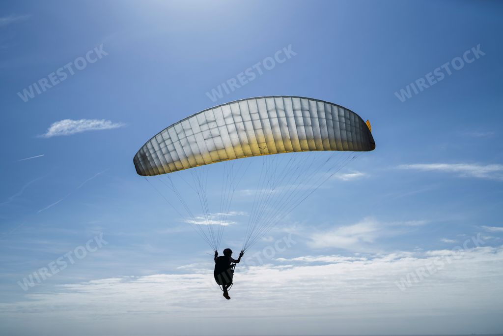 A closeup of a person Paragliding under the blue cloudy sky on a sunny day
