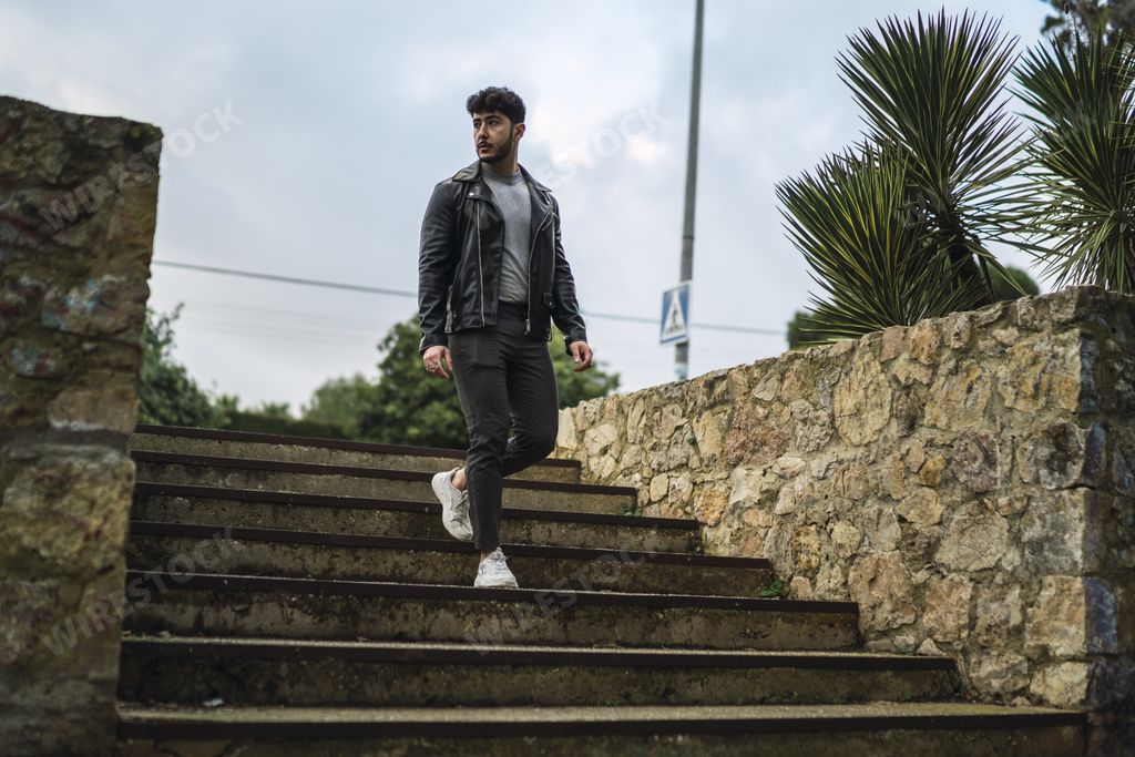 A shallow focus shot of a handsome European male in a black leather jacket walking down the stairs