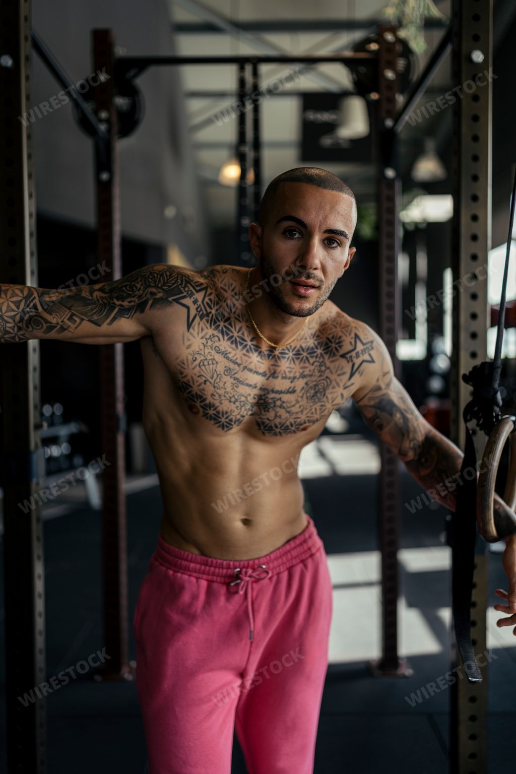 A young, tattooed male with a fit physique poses in a gym
