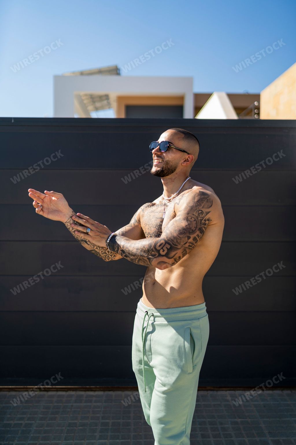 An athletic cheerful man is demonstrating his chest and arms with black tattoos