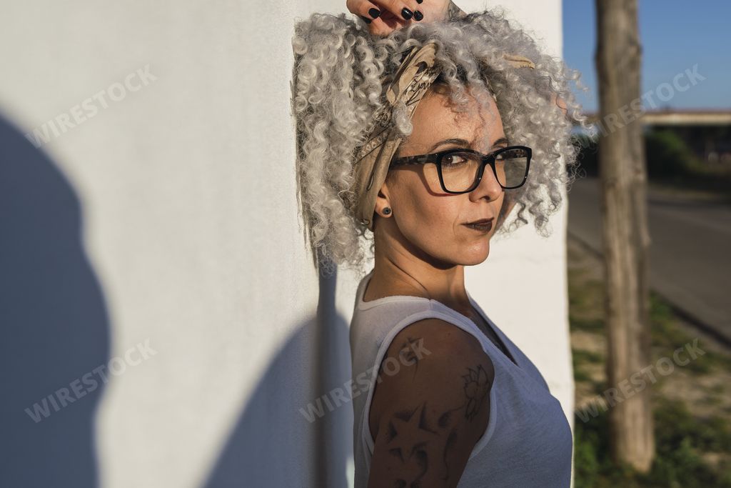 A curly-haired Spanish cute woman with tattoos on a white wall background