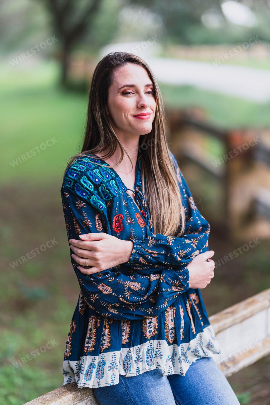 A young woman with her arms crossed leaning against a railing, looking intently at the camera with an enigmatic expression