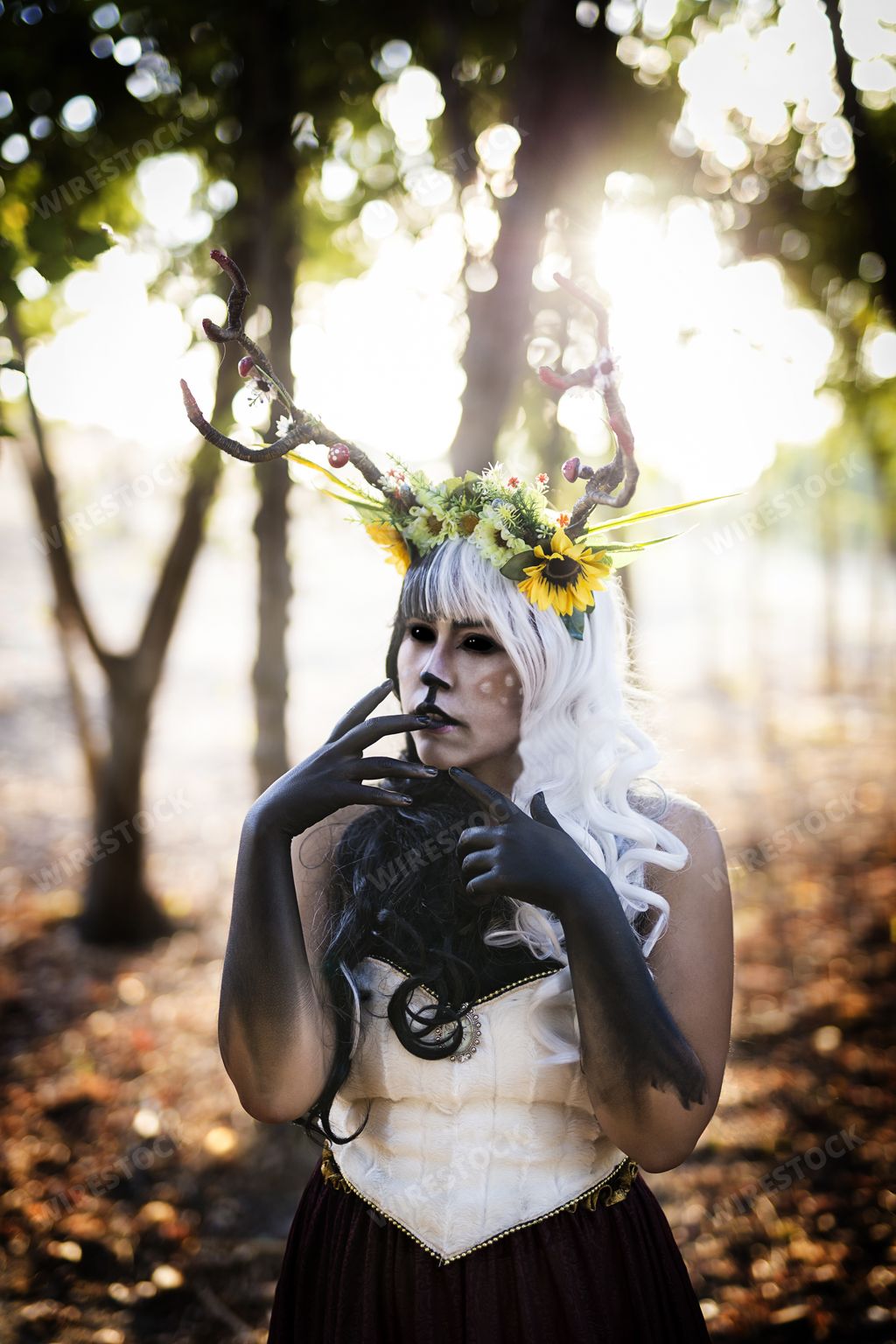 A vertical shot of a woman with deer antlers flowers  and makeup in the forest