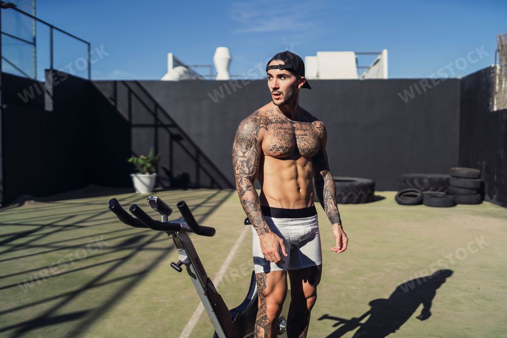 An attractive caucasian muscular man in tattoos standing near an exercise bike