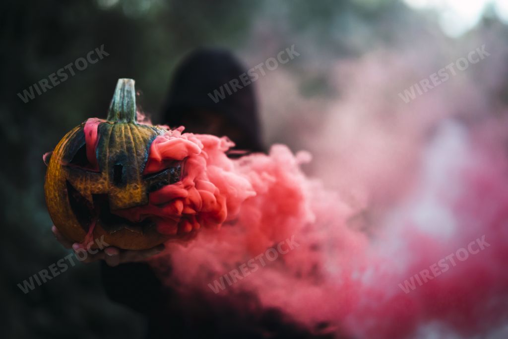 A man holding a carved pumpkin with red smoke - the concept of Halloween