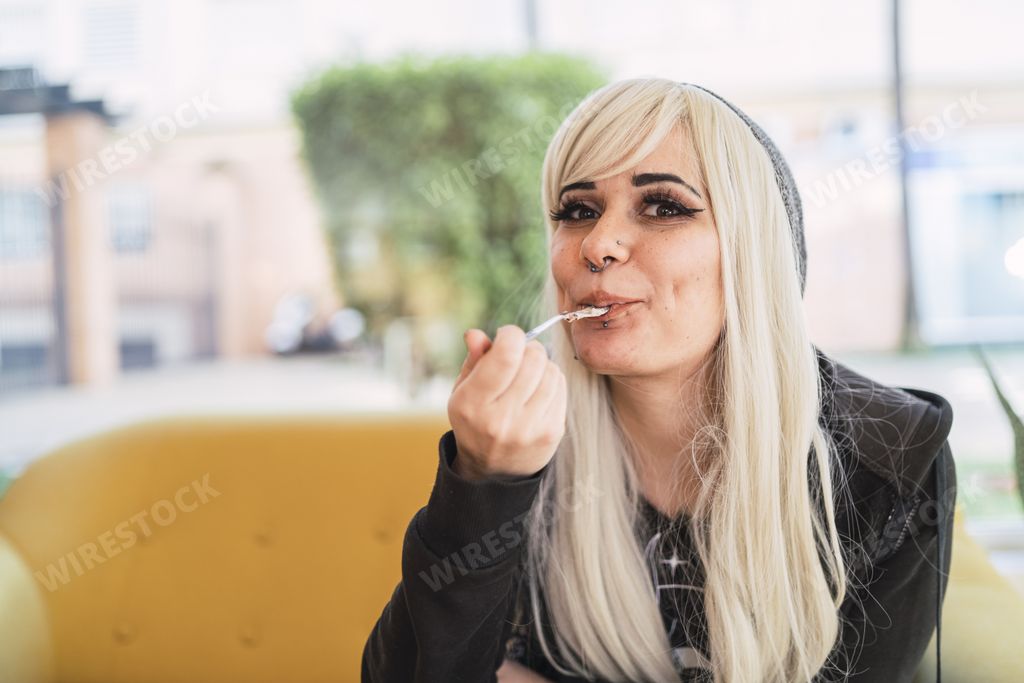 A blonde female with a nose ring sitting in  cafe with a spoon in her mouth