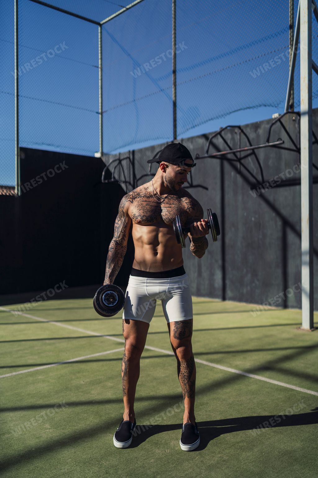 A Caucasian handsome man with tattoos training with dumbbells