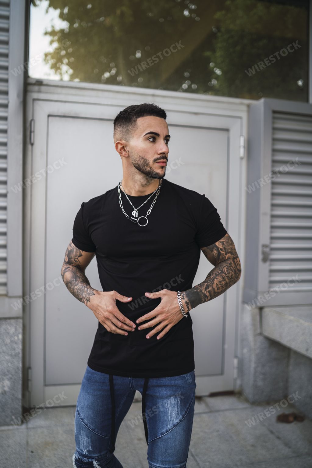 A sexy tattooed man wearing a tight black shirt and jeans standing on the background of a gate
