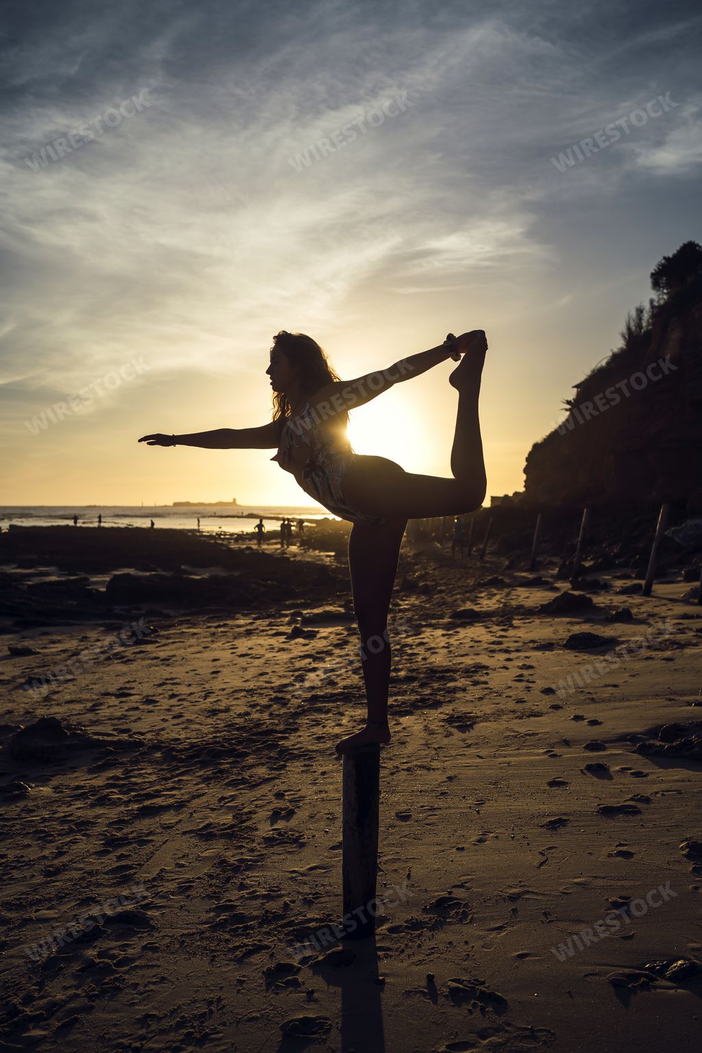 A vertical shot of a female doing the standing bow pose in the evening on the Chiclana beach, Spain