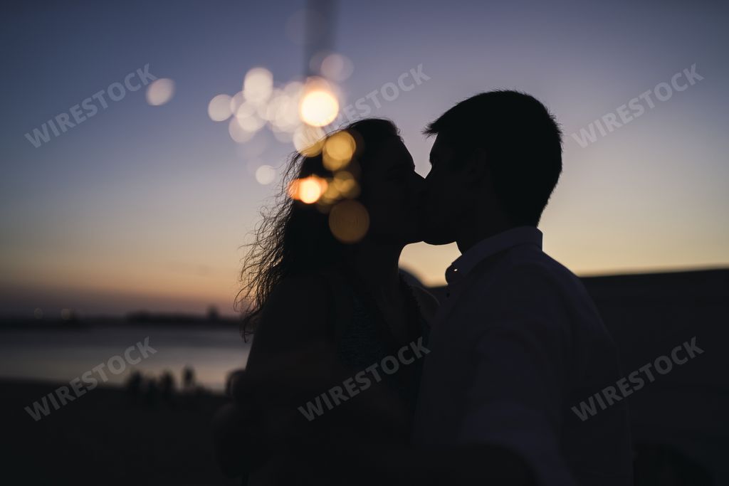 A silhouette of a young couple kissing at sunset; an image with bokeh lights effect