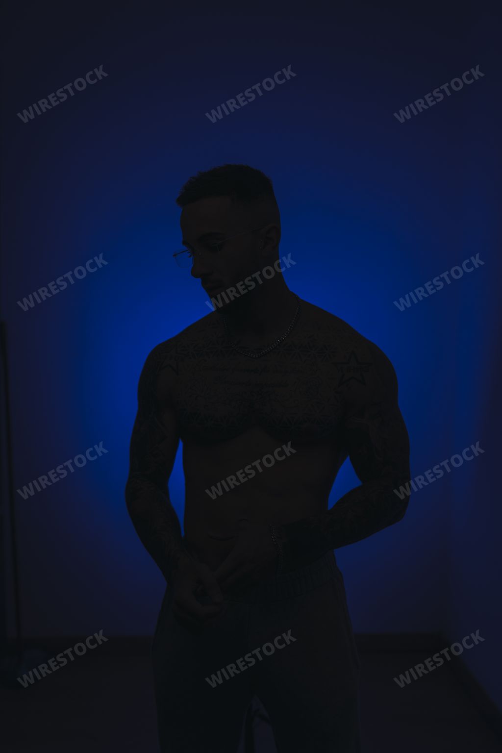 A sexy young shirtless Spanish male posing in a dark room with blue lights