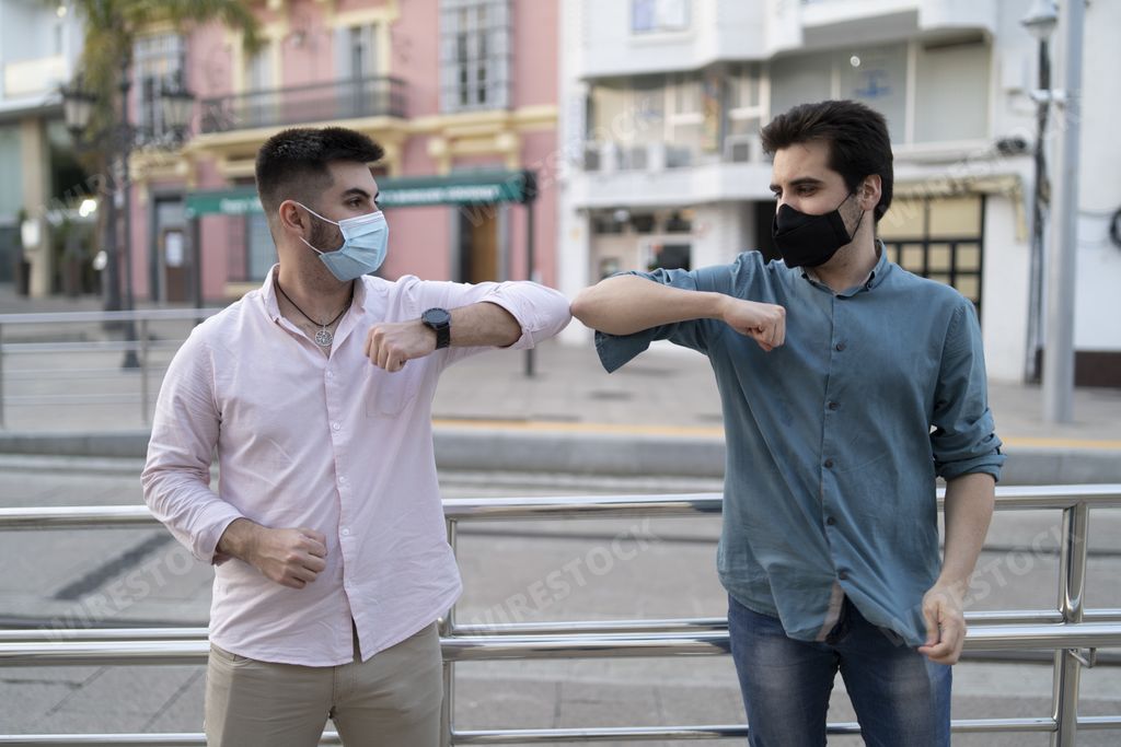 Handsome Spanish men wearing masks and greeting each other with elbows - new normal concept