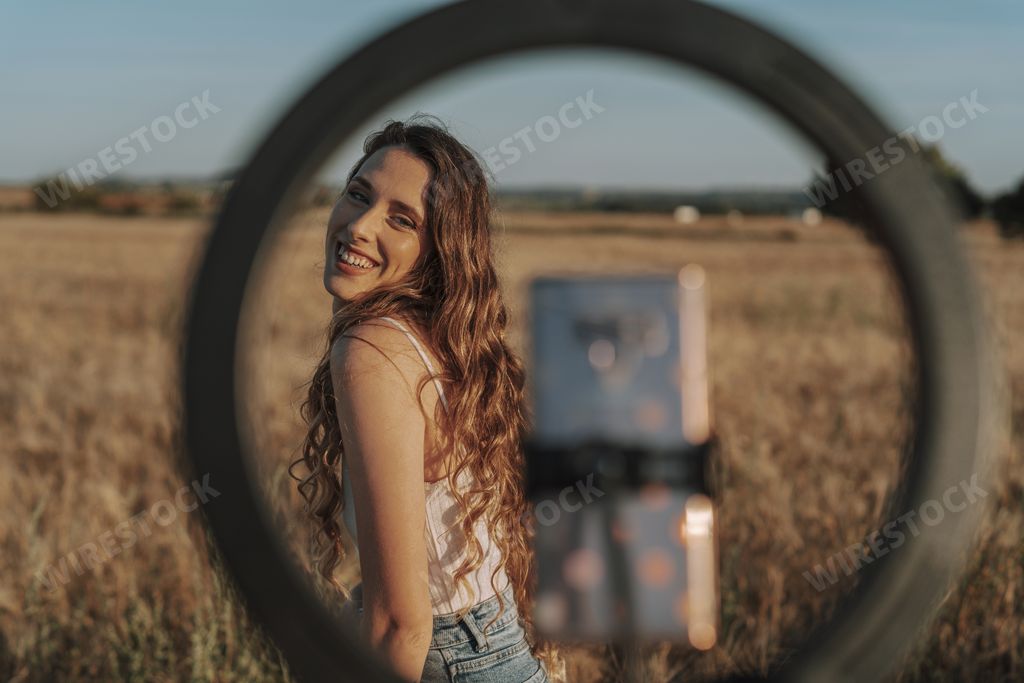 A gorgeous Spanish woman smiling at her phone while taking a selfie with it attached to a ring light
