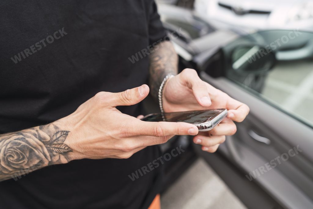 Male hands with tattoos holding a phone near the car