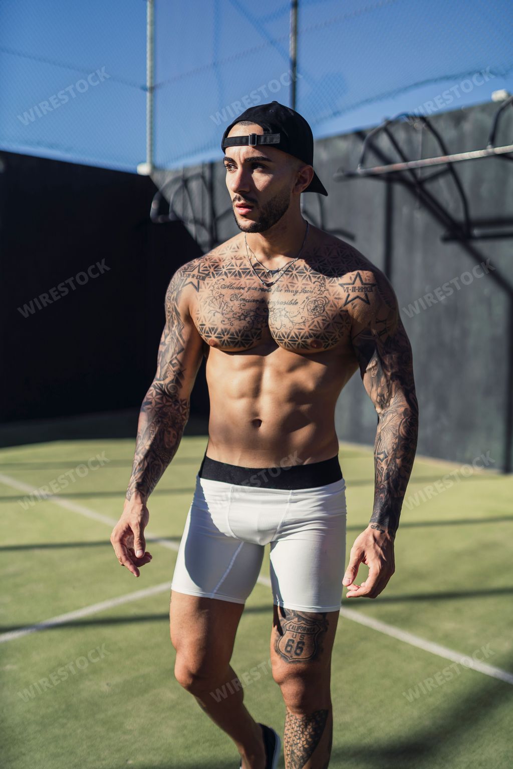 A vertical shot of an attractive shirtless tattooed man wearing boxers and a hat in an outdoor court