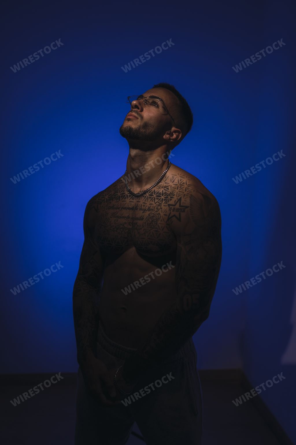 A sexy young shirtless tattooed Spanish male posing in a dark room with blue lights