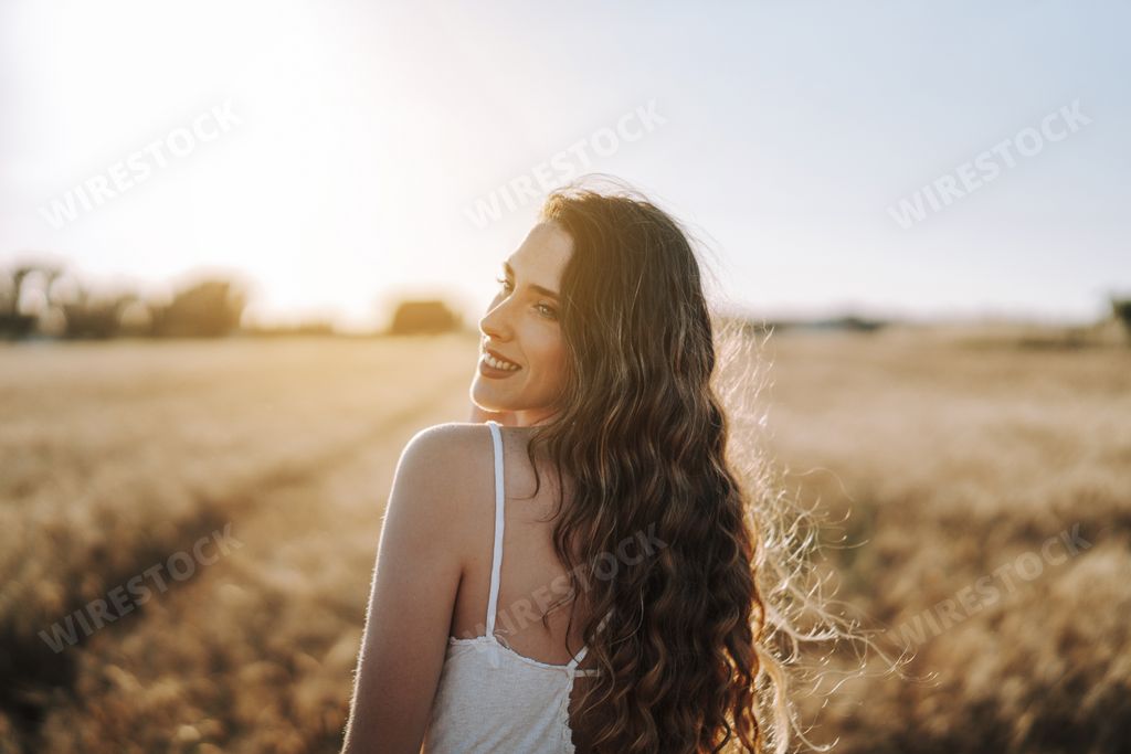 A gorgeous blonde Spanish girl smiling happily with the sun shining behind her in a wheat field