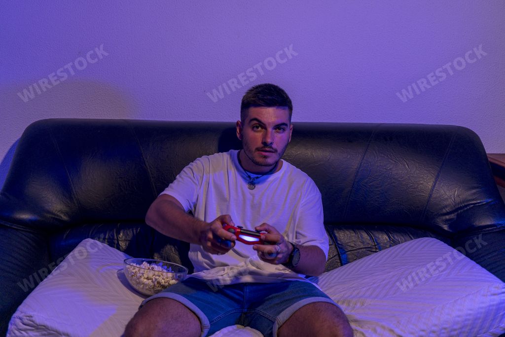 A closeup shot of a young man sitting on a couch with a joystick playing a video game