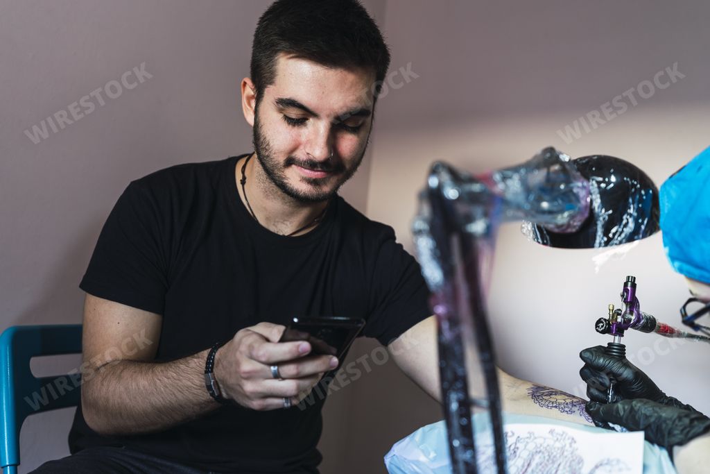 A man scrolling on his phone when getting his arm tattooed