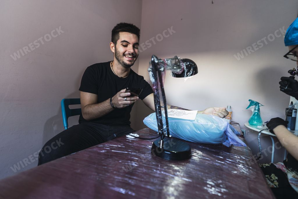 A man scrolling on his phone when getting his arm tattooed