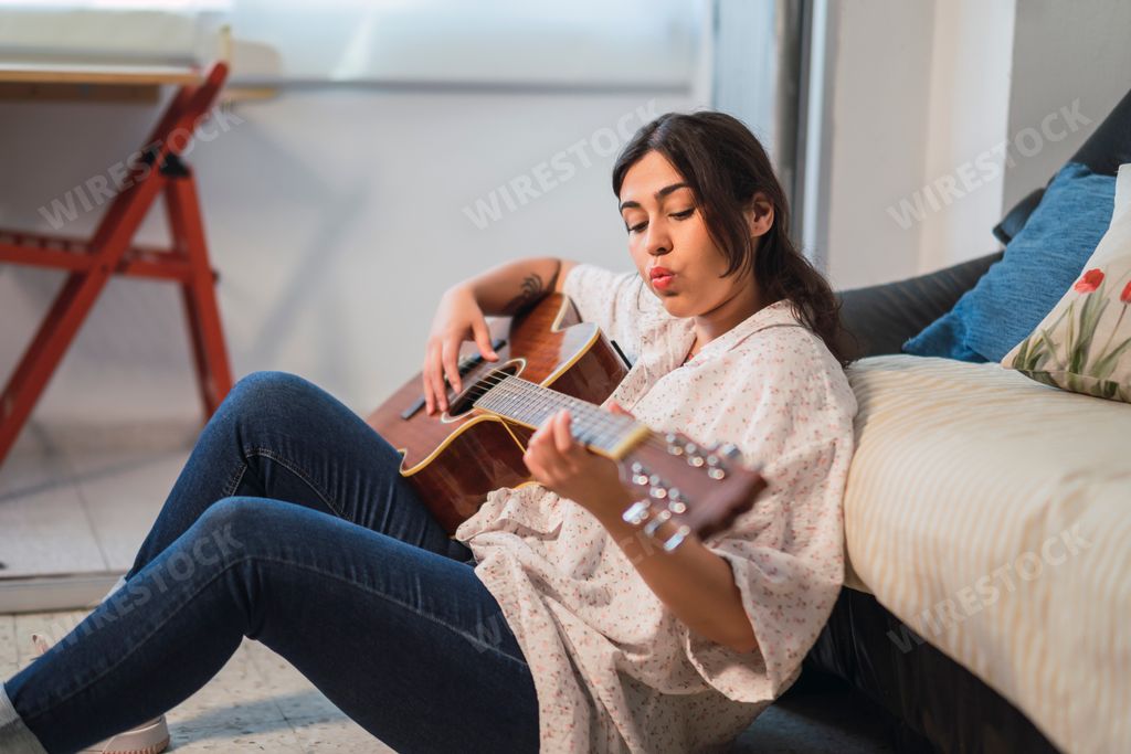 A beautiful shot of a girl whistling and playing guitar on the ground