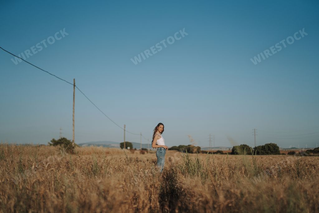 A blonde Spanish girl standing under a hot, cloudless blue sky in a sunny wheat field