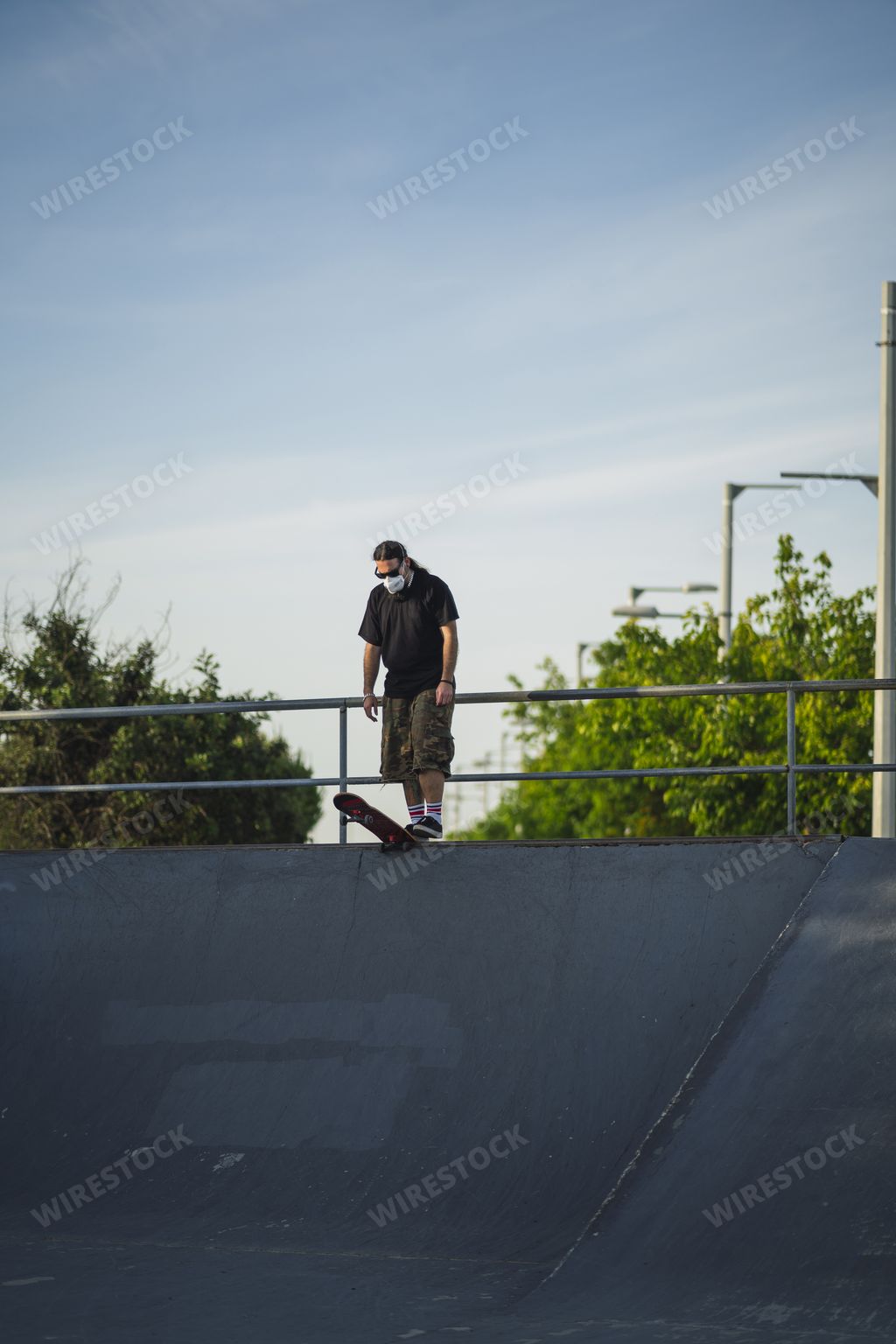 A young male walking in a park with a skateboard wearing a medical face mask - Covid-19 concept