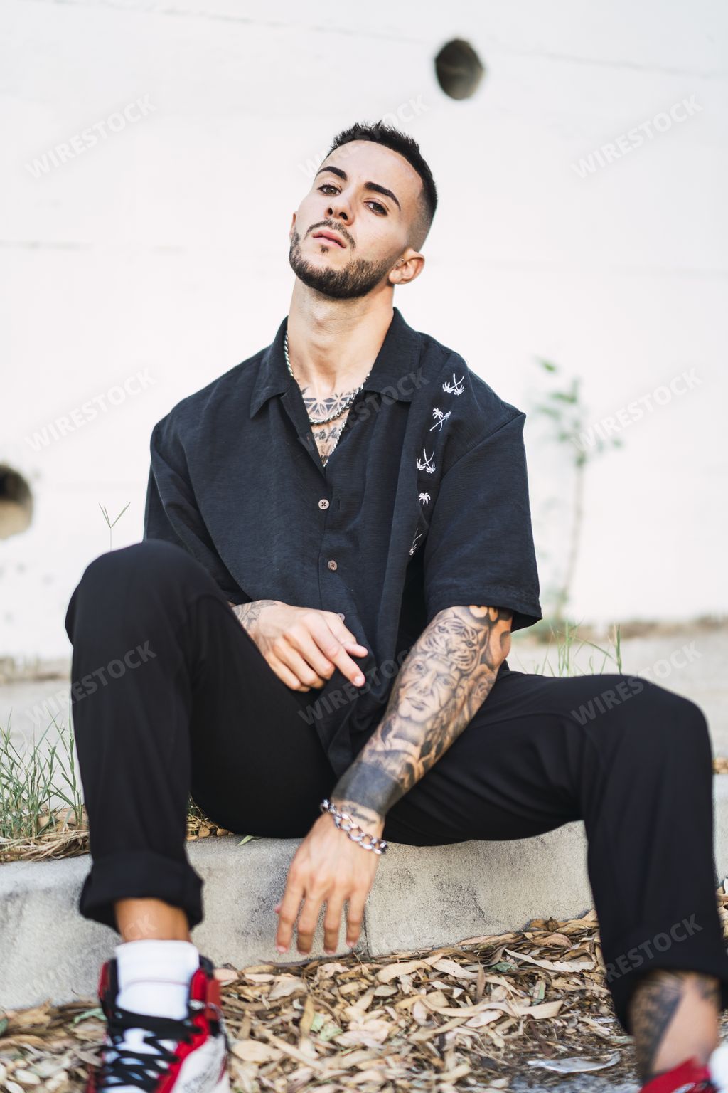 A vertical shot of a handsome male with tattoos sitting by a building