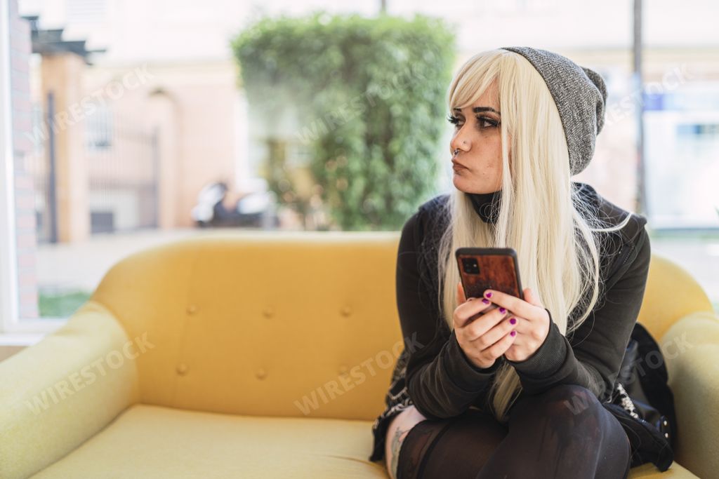 A young blond Spanish woman with a phone in her hands and a mask under her chin looking to the side
