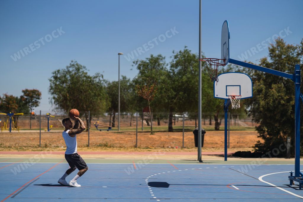 A young sporty guy on the outdoor basketball court throwing the ball to the hoop